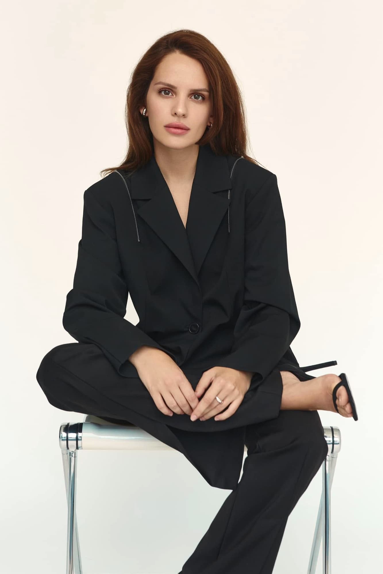 Anna Bon seated, in a black suit against a pale background.