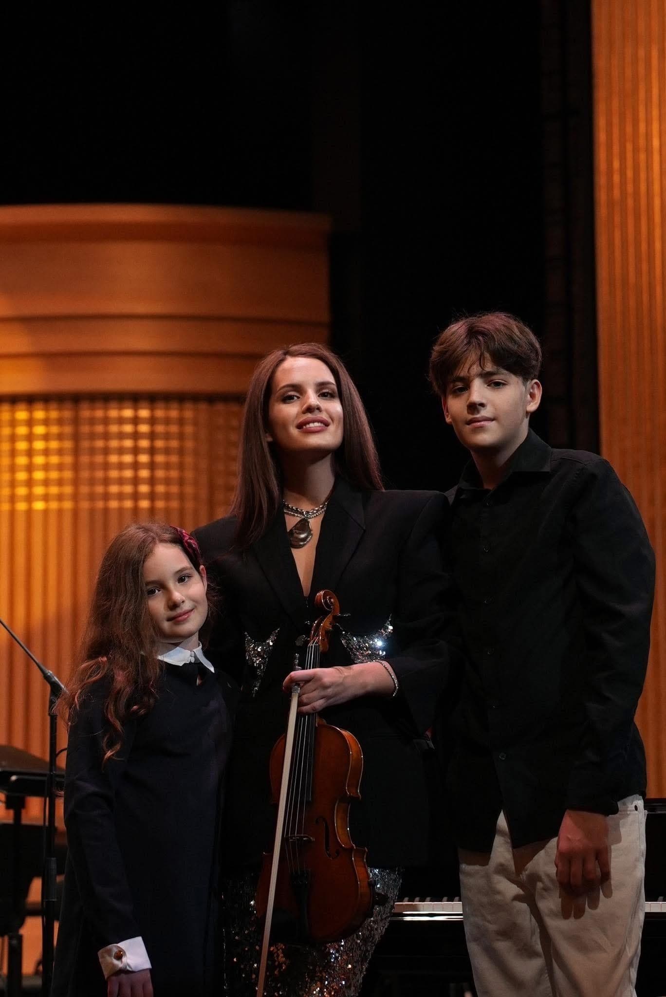 Anna Bon on stage with her violin, with two young musicians beside her.