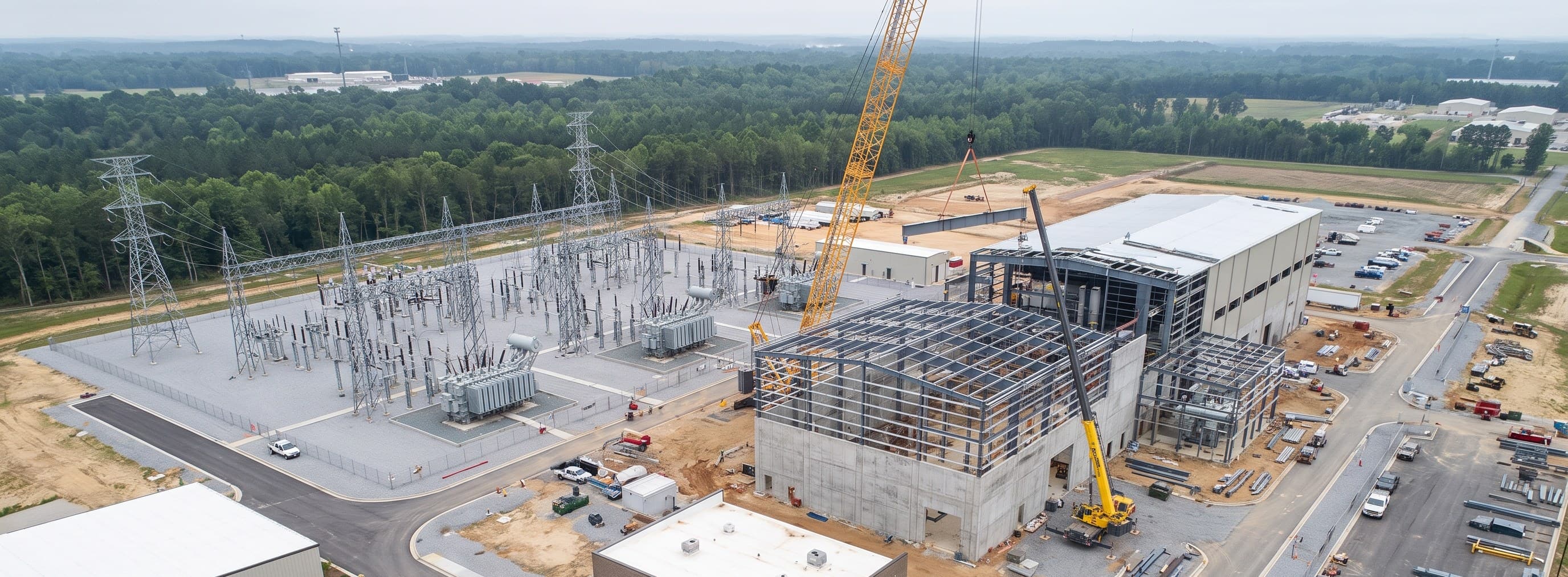 A high-voltage substation beside the steel frame of a building under construction, a crawler crane above it.